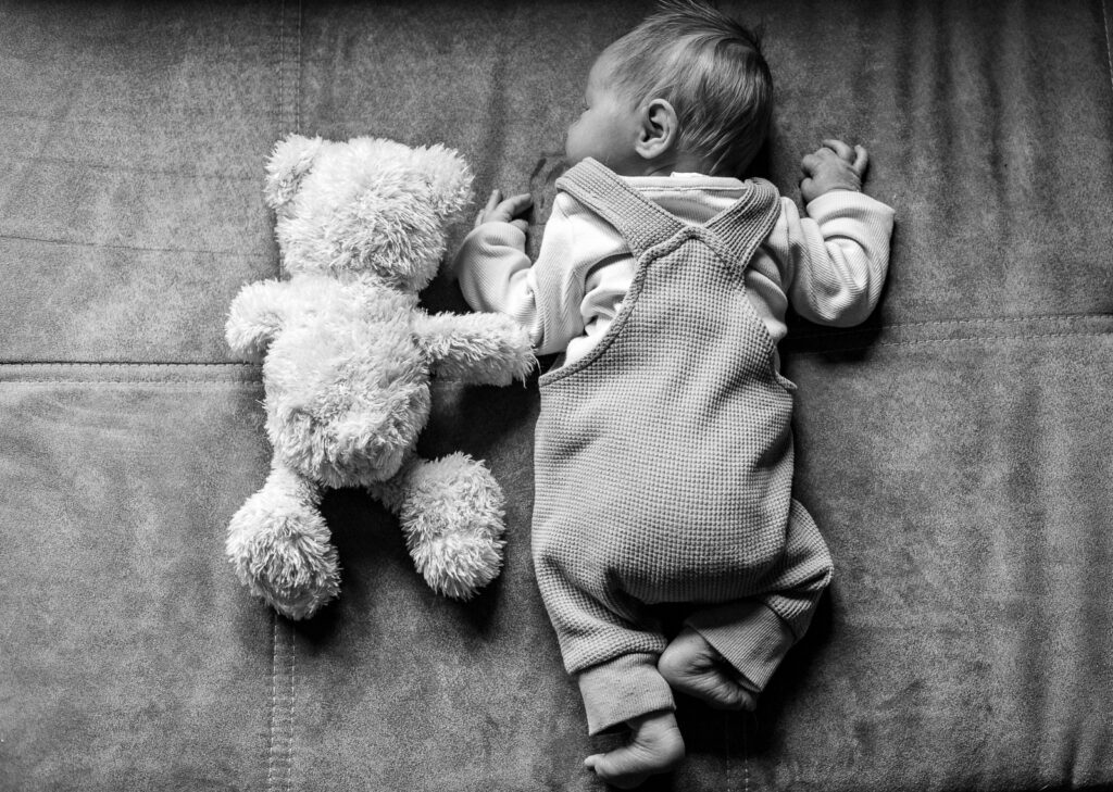 Baby liegt neben einem Teddybär auf dem Sofa – liebevolle Familienfotografie im Saarland