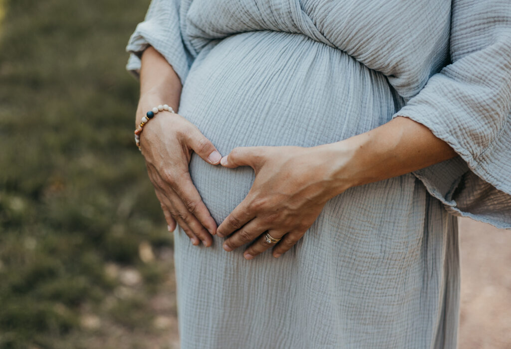 Hände formen ein Herz auf einem Babybauch bei einem emotionalen Schwangerschaftsshootin