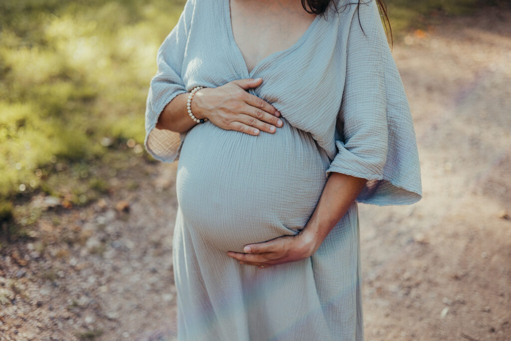 Schwangere Frau hält liebevoll ihren Babybauch bei einem Outdoor-Shooting im Abendlicht