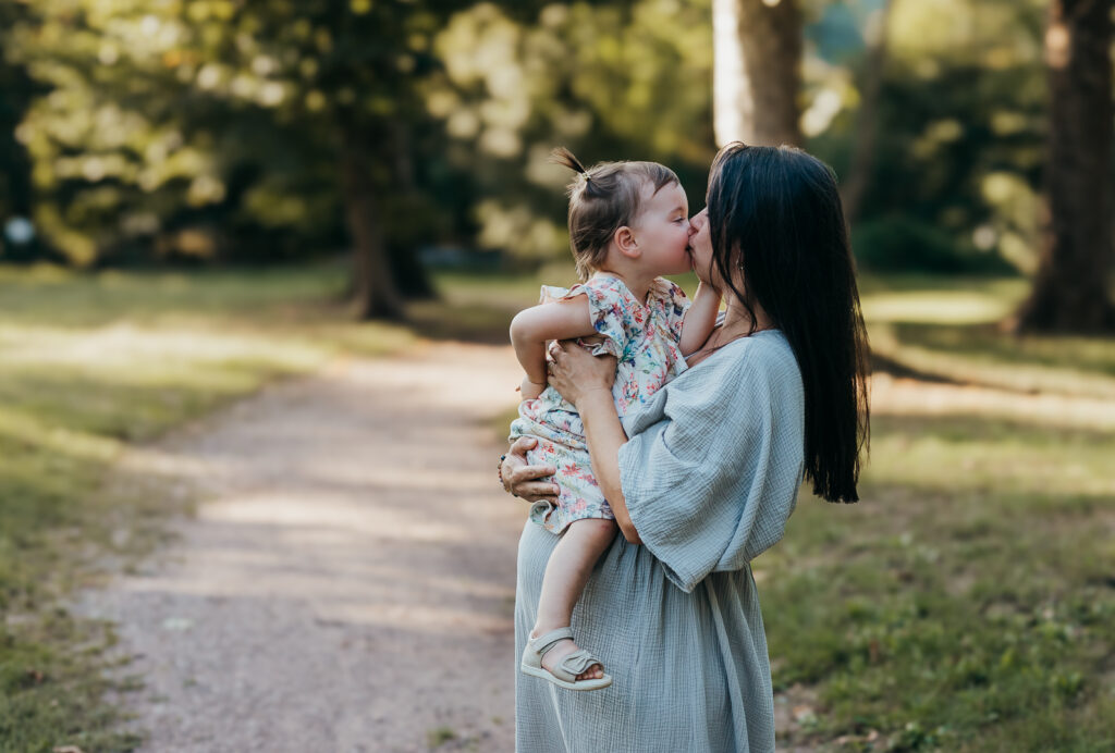 Mama hält ihr kleines Kind im Arm und gibt ihm einen liebevollen Kuss bei einem Spaziergang in der Natur