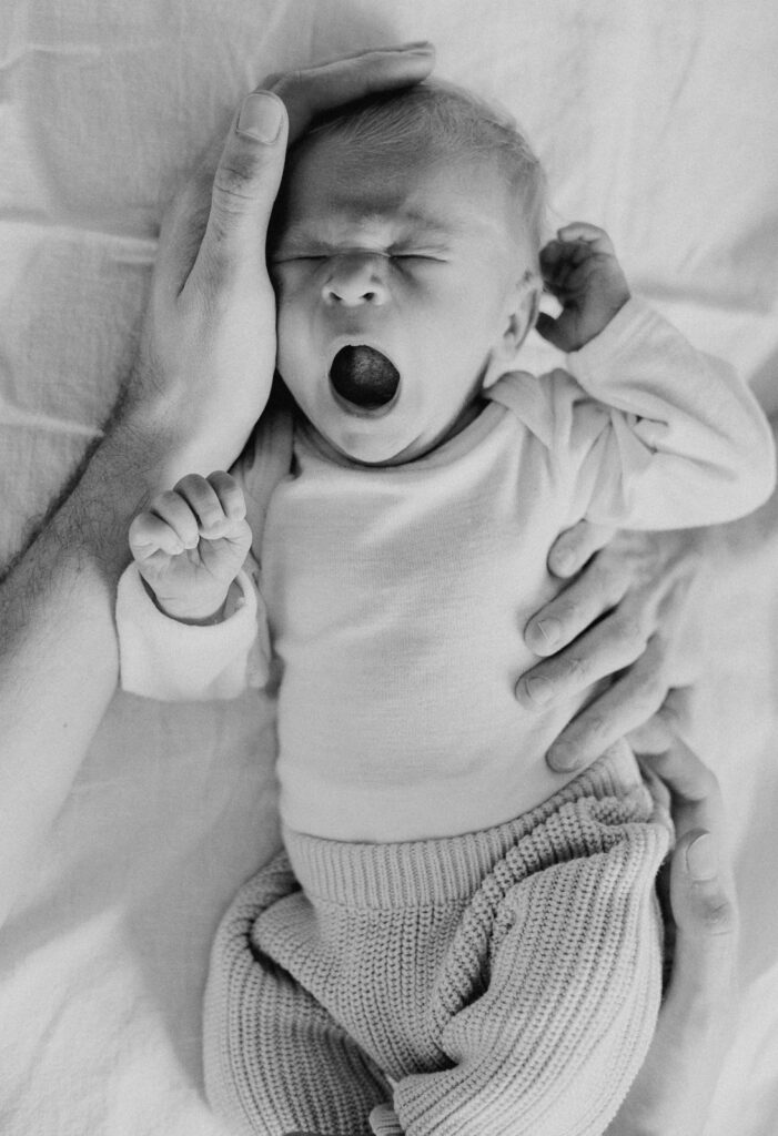 Neugeborenes liegt geborgen in den Händen der Eltern und gähnt entspannt