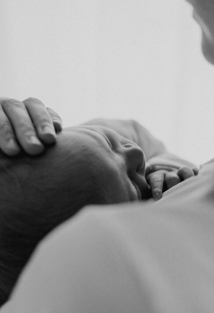 Neugeborenes liegt geborgen auf der Brust der Mutter in einer emotionalen Schwarzweißaufnahme
