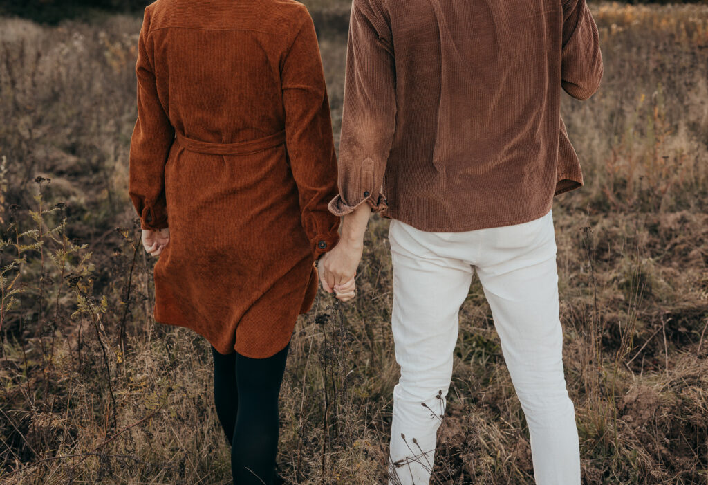 Paar läuft Hand in Hand durch eine herbstliche Naturkulisse von hinten fotografiert