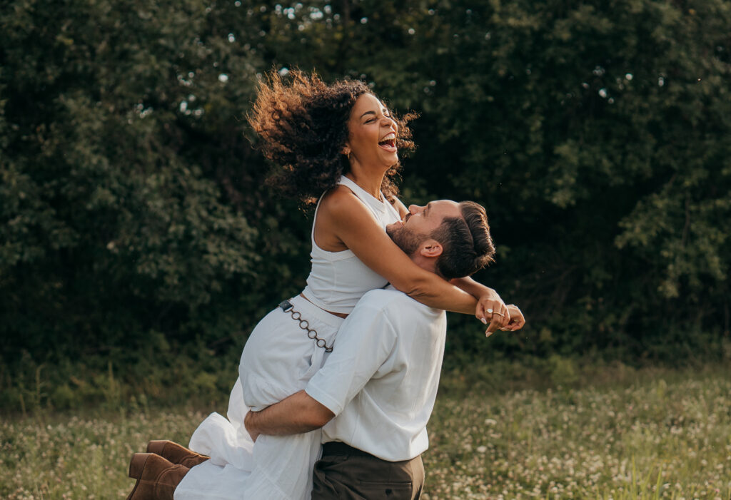 Mann hebt seine Partnerin lachend hoch bei einem Paarshooting auf einer Wiese im Saarland