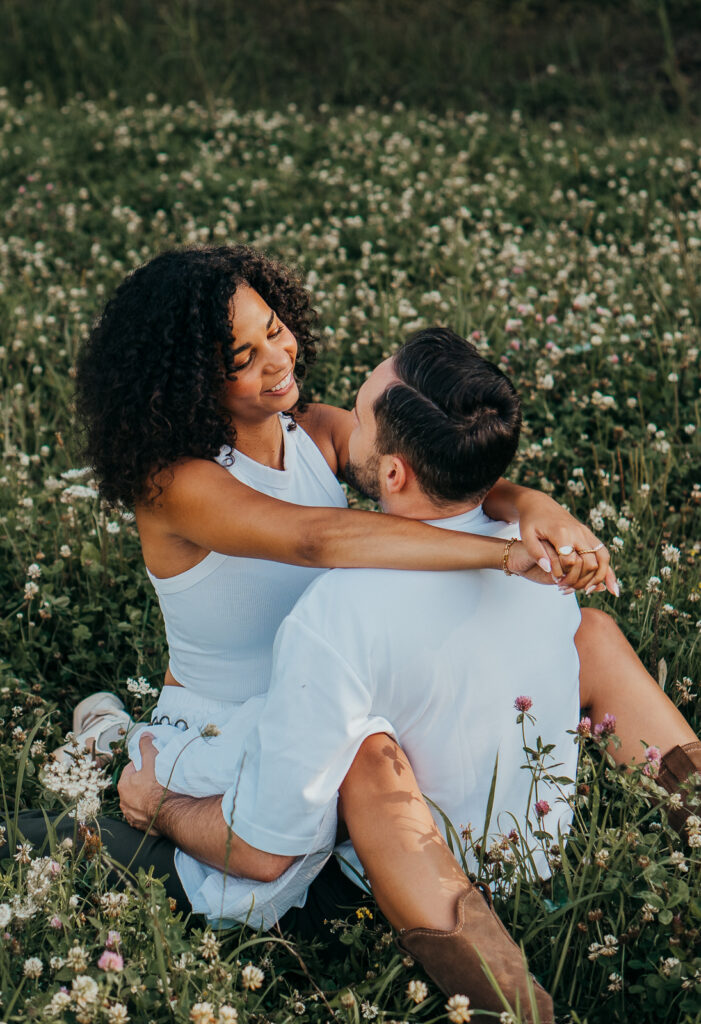 Verliebtes Paar sitzt eng umschlungen in einer blühenden Wiese beim Outdoor-Shooting