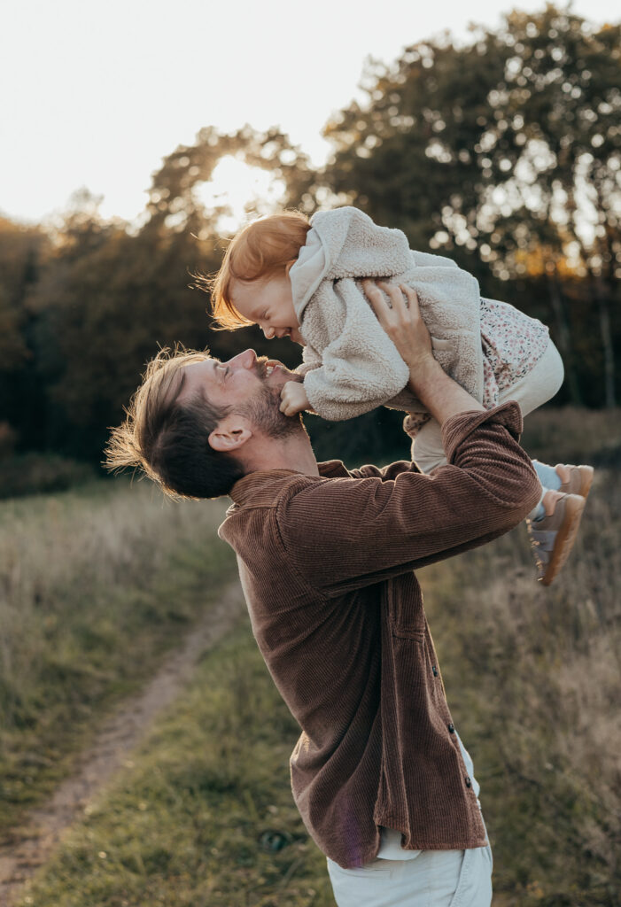 Vater hebt sein Kind lachend in die Luft bei einem Familienshooting im warmen Abendlicht