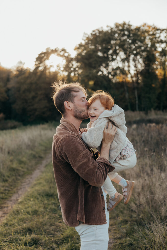 Vater gibt seinem lachenden Kind einen liebevollen Kuss bei einem Outdoor-Fotoshooting